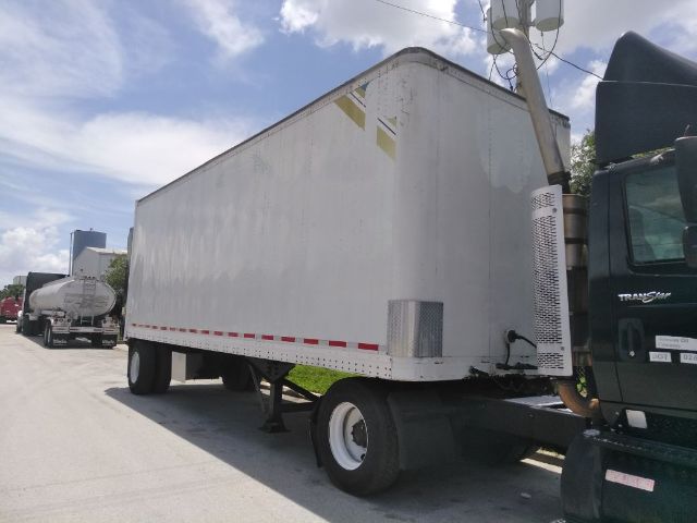 Trailer box attached to a semi truck with white aluminum sides, rear wheels, and a cab visible on the right side.