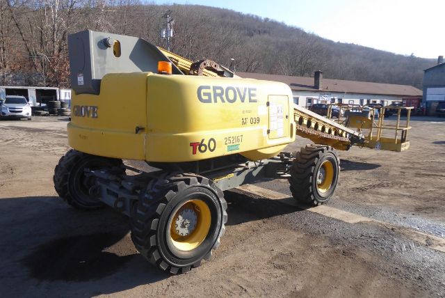 Grove T60 mobile crane in a yard showing yellow body with 'GROVE' and 'T60' markings, rear wheels, and a long telescoping boom extended. Visible text includes 'GROVE' on side, 'T60' near the rear, and small labels/stickers on the body.