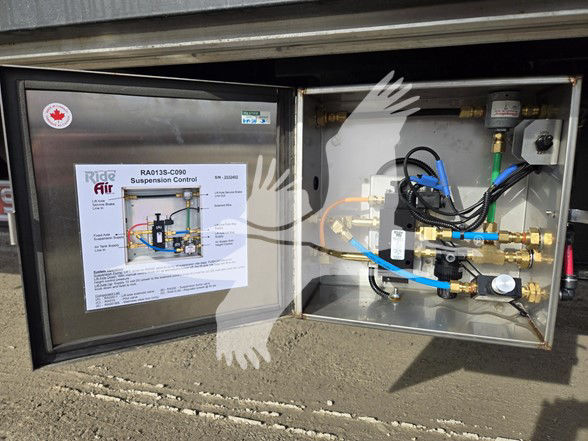 RAIDE AIR suspension control diagram in the left panel; a hydraulic manifold with blue and yellow PEX lines, brass fittings, gauges, and wiring inside a metal cabinet on a drop deck trailer.