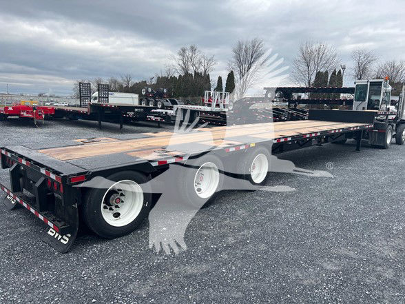 Steel drop trailer with three axles and middle lift, long flatbed in an outdoor lot.