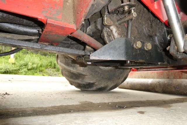 Underbelly of red Steiner 415 agricultural equipment with large wheel and black metal brackets visible; dirt and ground beneath.