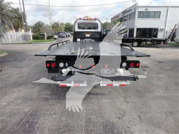 Tow truck with flatbed rear, International MV model, rear view showing taillights and hydraulic bed platform.