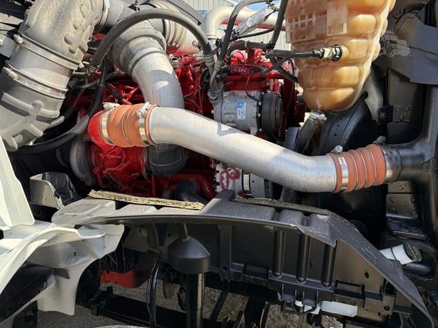 Truck engine bay showing red engine block with large gray turbo intake pipe and hoses, beige coolant reservoir, and surrounding components.