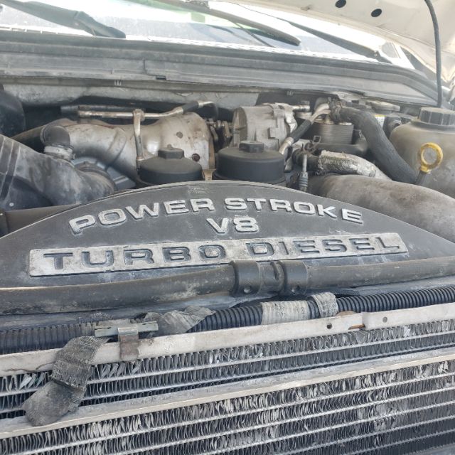 Ford F-550 engine bay showing Power Stroke V8 Turbo Diesel decorative lettering on engine cover. Visible components include radiator grille, hoses, and engine bay layout.