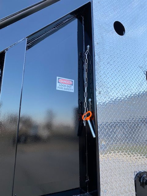 Trailer deck with safety latch and chain,5088 Transcraft logo sticker on glossy black surface, diamond plate steel at edge.