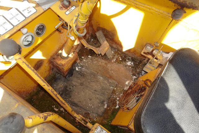 Interior of Grove RT58 crane cab showing yellow control levers, gauges, pedals, and worn floor with operator seat.