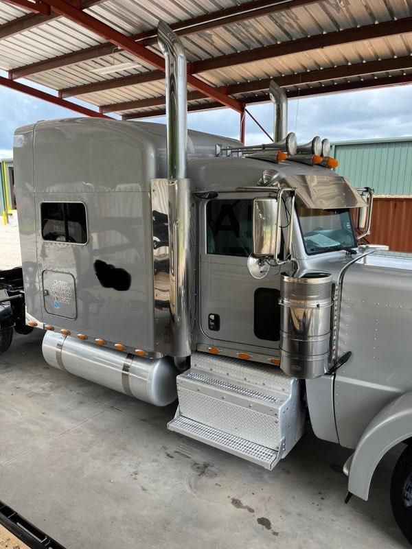 Peterbilt conventional sleeper truck in a silver finish showing side steps, elevated exhaust stacks, chrome fuel tanks, and a chrome air filter canister.