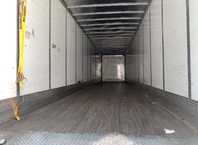 Interior of an empty utility trailer cargo area with metal walls and a wooden floor, tie-down strap visible on left side.
