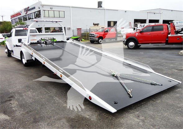 Flatbed tow truck bed on a Ram 5500 chassis with loading ramps and safety chains.