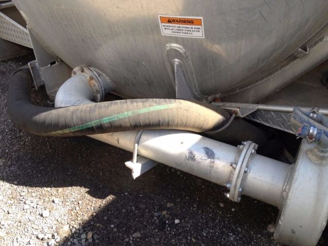 Tank truck vacuum tank with large metal tank and connected hoses; warning label visible on the tank near a curved pipe and flange.