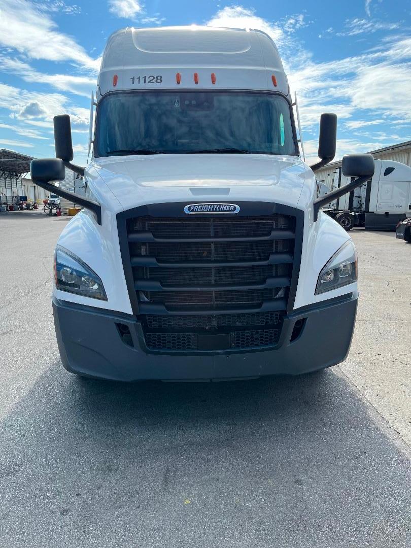 Front view of a white 2021 Freightliner Cascadia 126 conventional sleeper tractor showing large black grille, headlights, and side mirrors.