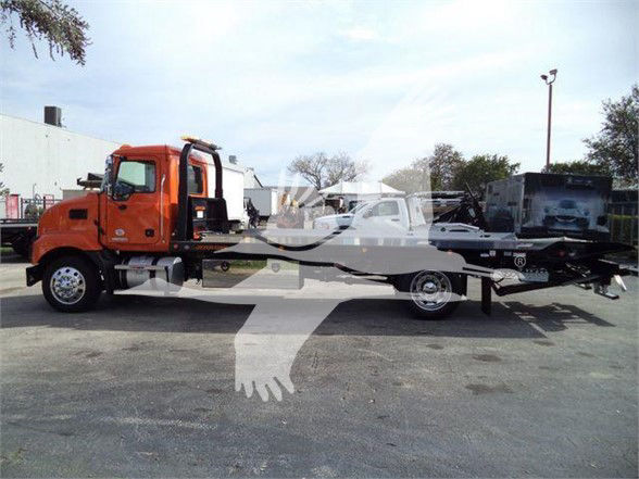 2024 Mack MD6 tow truck in orange cab with flatbed, side view showing cab and elongated bed with wheel hubs and a hitch.