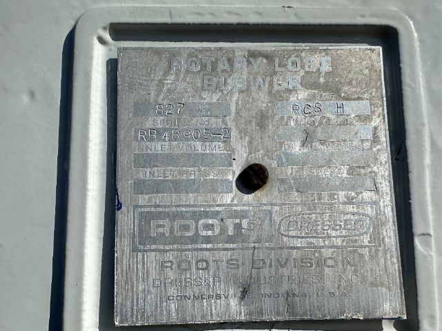 Flat metal identification plate on a Roots power unit with embossed text and hole in center, showing model and capacity details.