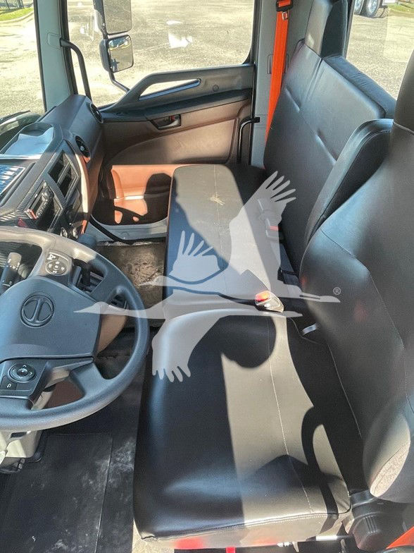 Truck cab interior showing driver seat, steering wheel with logo, dashboard, and bench seating in black upholstery.