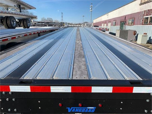 Vanguard 48ft steel flatbed trailer viewed from rear with metal ribbed deck and reflective red-white tape along edge; Vanguard logo on bumper.