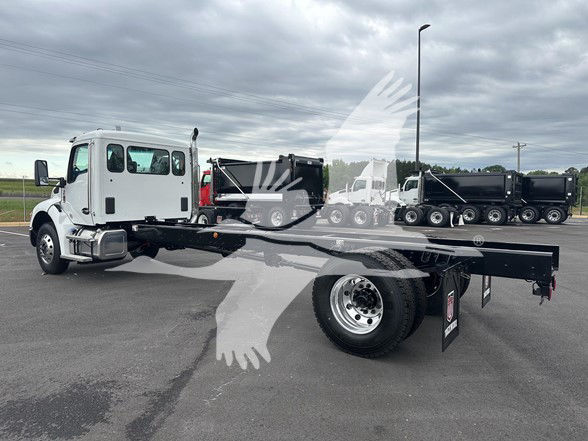 Kenworth T380 cab and chassis in a parking lot with flatbed, white cab, black chassis, truck tires, other trucks in background.