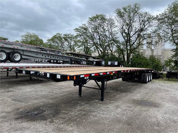 Fontaine flatbed trailer with extendable all-steel deck, 53' to 90' length, shown in yard. Dual rear axles, support legs, reflectors along edge.