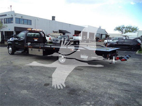 2023 Chevrolet Silverado 6500HD tow truck flatbed with black cab and extended flatbed, dealership lot in background.