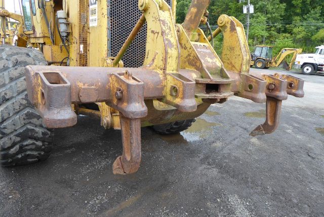 Turret view of a Caterpillar 16G rear hitch with rusted lifting lugs and attachment points on the ground in a yard.