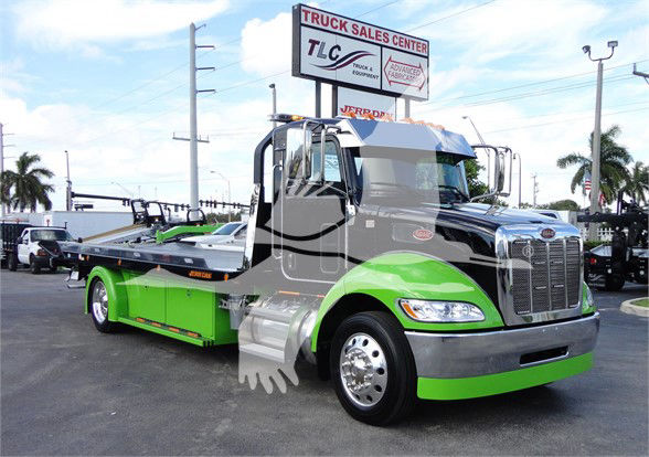 Peterbilt tow truck in green and black, front view, with stock number J56607 displayed on sign in background.