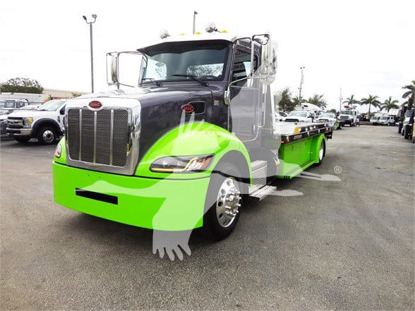 Peterbilt 337 tow truck with a bright green front and gray cab, chrome grille, and flatbed, parked in a lot.