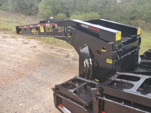 Lowboy trailer kingpin area and gooseneck with hydraulic arm and warning decals, black metal framework, yellow caution labels, textured surface and utility compartments.