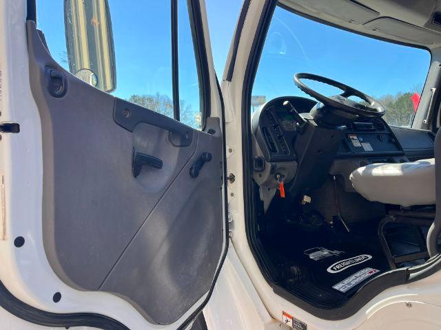 Cab interior of a 2018 Freightliner M2 106 dump truck showing the open driver door, steering wheel, dashboard, and floor mats.
