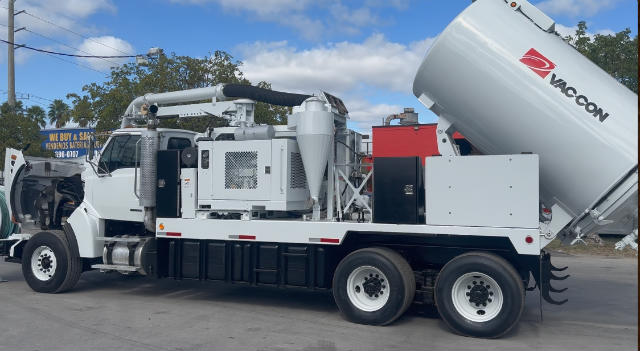 Large white truck-mounted vacuum excavation unit with a concrete pump hose and Vacon cement mixer attachment, showing tanks, engine bay, and rear dual wheels.