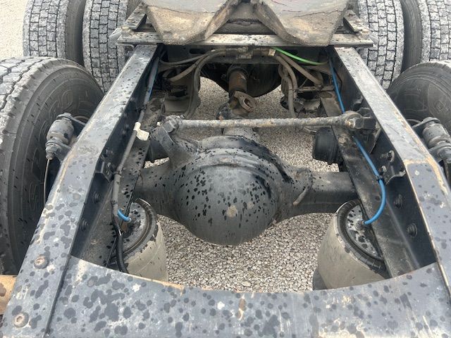 Truck chassis with rear axle and suspension components visible between dual rear tires; dirt and grime on metal differential housing and leaf springs.