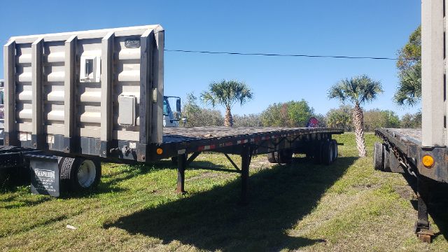 Flatbed trailer with a long gooseneck sections and tandem axles, Great Dane style, side view showing support legs and wheels.