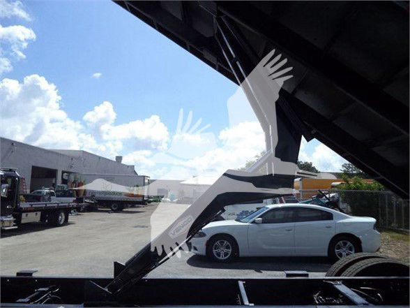 Truck dump bed frame visible with blue sky and white car in background.