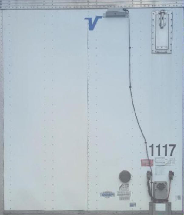 Rear of a Vanguard VXP trailer with VIN tag, stock number 1117, and utility trailer equipment; shows V logo, electrical plug, and side door.