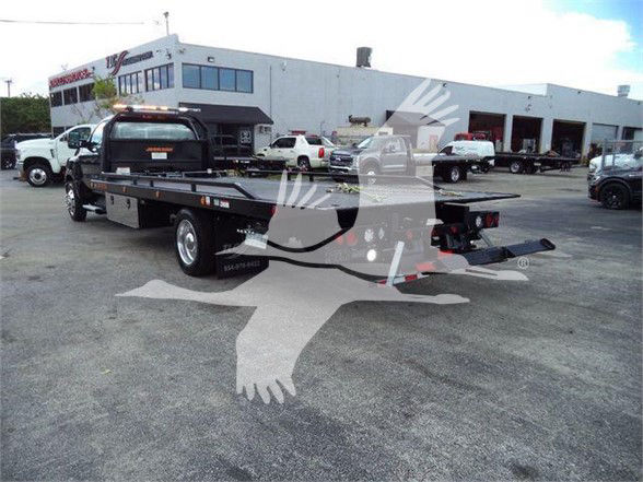 Flatbed tow truck in a dealership lot with white building in background.