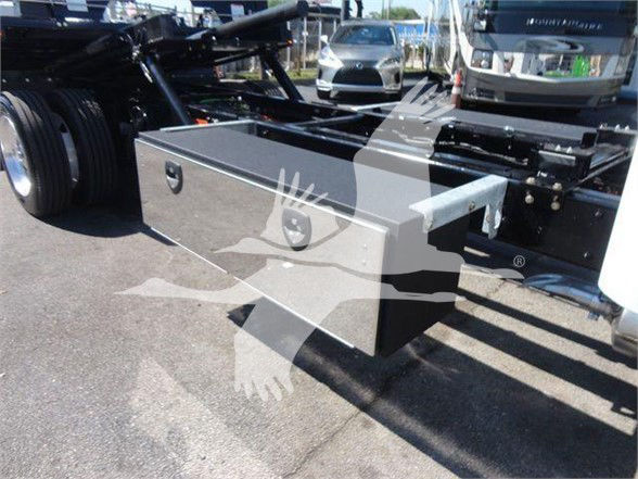 Flatbed truck chassis with a large rectangular toolbox mounted under the cab on a Freightliner M2 106 configuration.