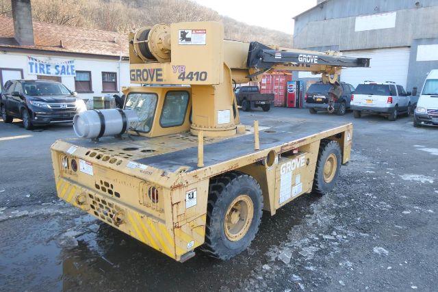 Grove YB4410 crane mounted on a yellow flatbed truck with a boom arm folded back, rear diesel engine area, and tires; visible stickers and labels.