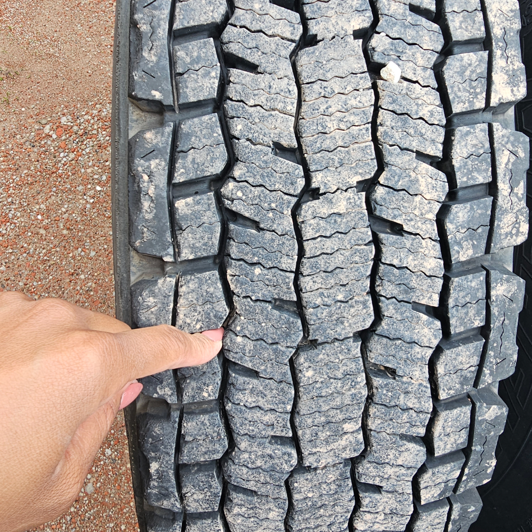 Tread depth on truck tire with a finger pressing into the tread, showing cracked and worn lug pattern.