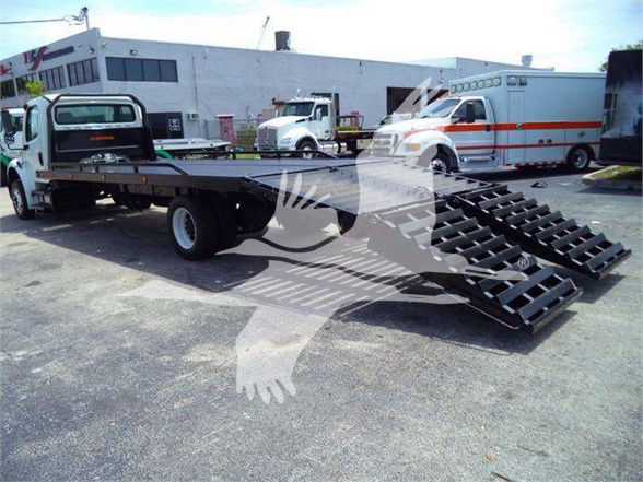 Flatbed tow truck with loading ramps extended, Freightliner Business Class M2 106 in background.
