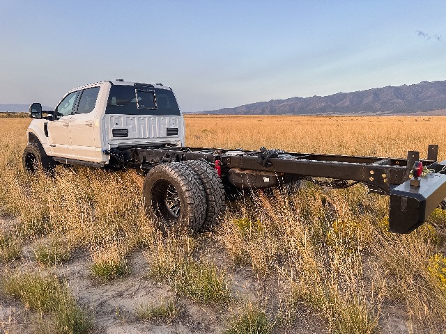 Side view of a white 2022 Ford F-550 Lariat cab and chassis with extended frame in a field, showing rear chassis and dual rear wheels.