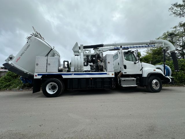 Vehicle side view of a white 2014 Freightliner 114SD vacuum truck with mounted machinery, hoses, and compartments. Visible text on equipment includes 'VAC-CON' on a large tank towards the rear of the bed.