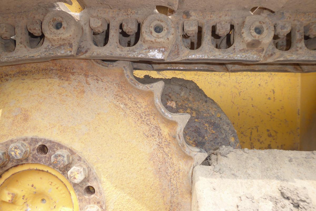 Tracks and sprocket of a John Deere dozer with yellow exterior, showing chain links and gear components with dirt and wear.