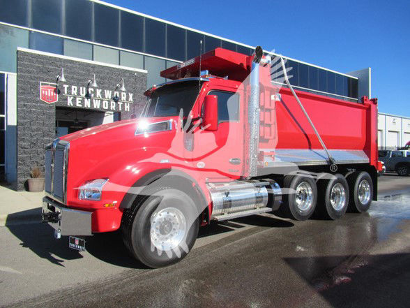 Kenworth T880 dump truck in red parked outside dealership with chrome fuel tanks and dual rear axles.
