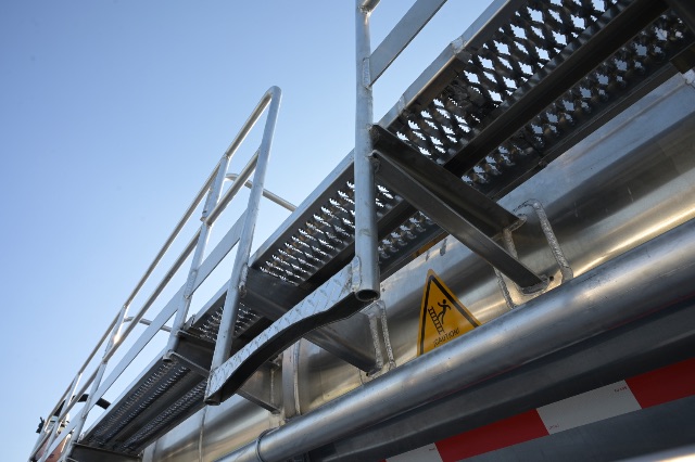 Trailer component showing aluminum vacuum tanker trailer with railing and caution sticker on the cylindrical tank.