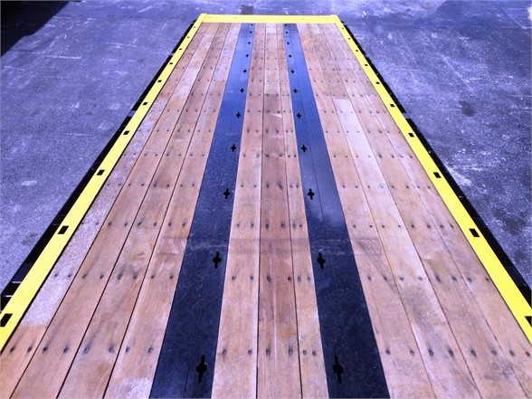Flatbed trailer or platform with wooden planks and black stripes, viewed from above. No visible text on the trailer itself.
