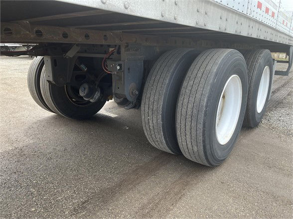 Trailer axles and wheels under a Vanguard VXP trailer showing triple-axle configuration with white rims and black tires.