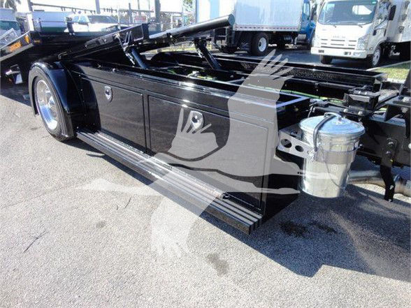 Truck chassis with side-mounted storage boxes and hydraulic components; polished black frame, fuel/coolant canister on the side, rear suspension and cab area visible.