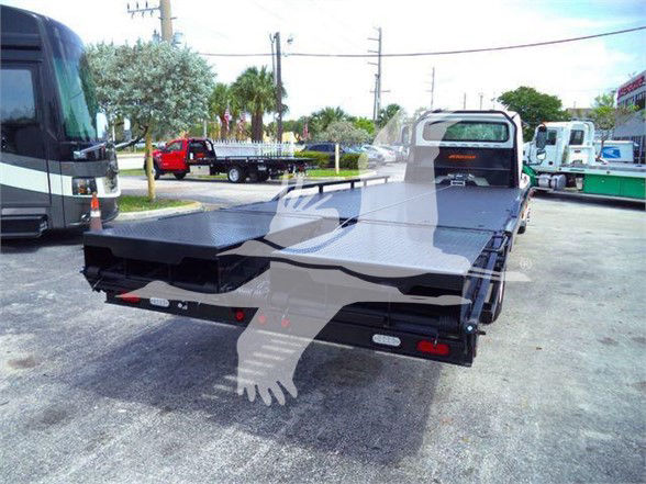 Flatbed Freightliner M2 106 rear view showing flatbed platform with taillights and hitch, truck cab in distance, outdoor lot.