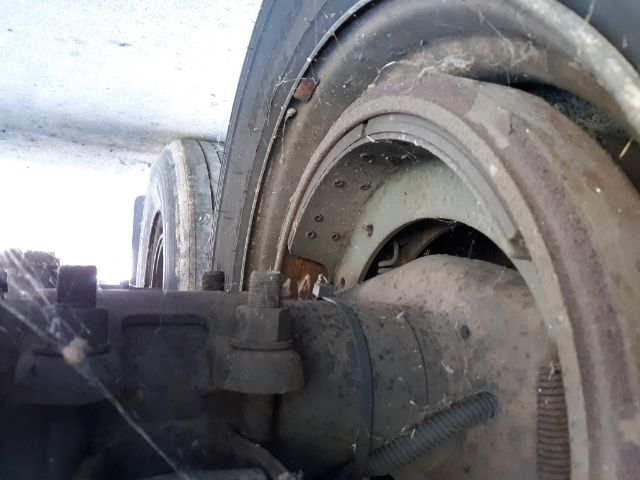 Rear wheel and suspension area of a utility trailer showing a dusty rim and tire, with undercarriage components visible.
