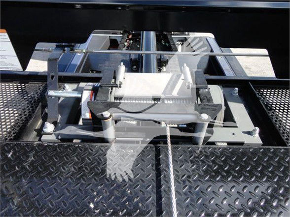 Tow truck hitch mechanism with metal roller and cable assembly on diamond plate surface.