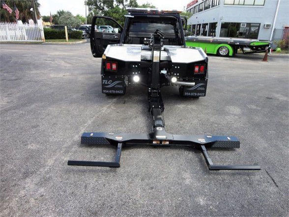 Ram 4500 flatbed tow hitch attached to a truck with a heavy steel hitch arm extending to the ground. Back of truck open doors visible; equipment and trailer hitch components laid out.