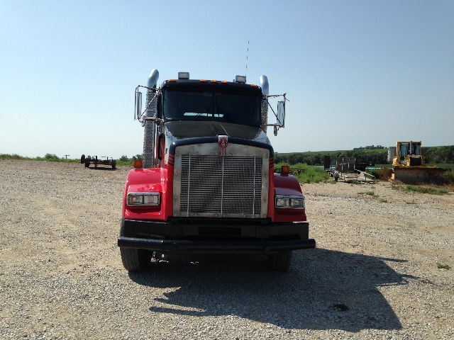 Front view of a red 2009 Kenworth T800 conventional daycab truck with large chrome grille and bumper, in gravel lot.